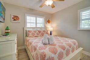 A bedroom with a bed, a desk, a ceiling fan, and artwork on the walls.