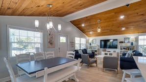 Un espacio habitable amplio con una mesa de comedor, sillas blancas, un sofá y un televisor.