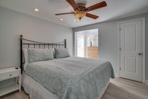 A bedroom with a bed, a nightstand, a dresser, a ceiling fan, and a door.