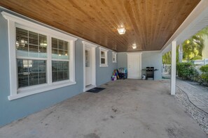 A covered patio area with a concrete floor, large windows, and a wooden ceiling.