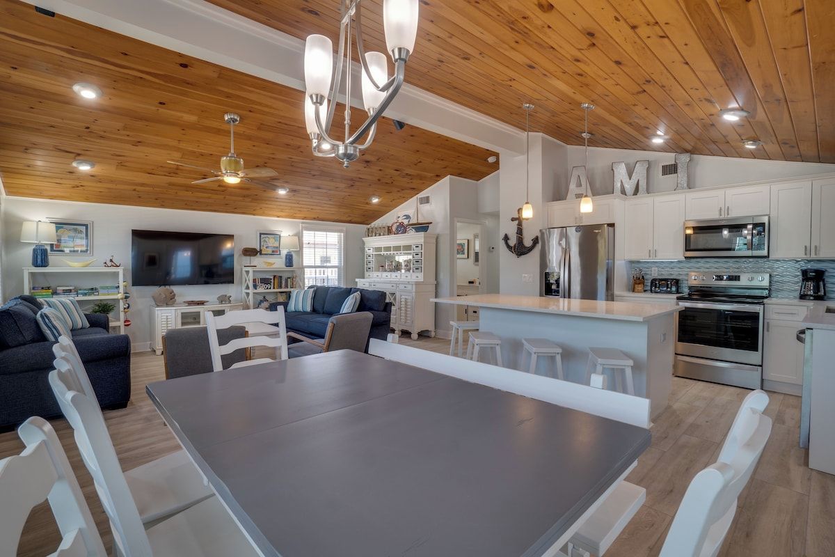 Une cuisine moderne avec des meubles blancs, un îlot central et un coin repas comprenant une grande table et des chaises blanches.