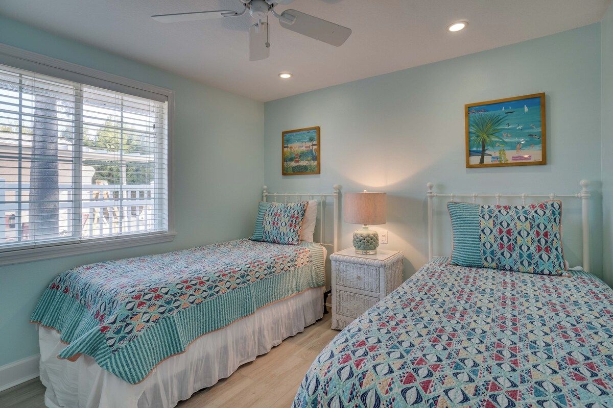 A bedroom with two beds, a ceiling fan, and a window with blinds.