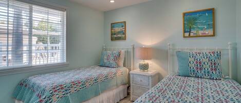 A bedroom with two beds, a ceiling fan, and a window with blinds.