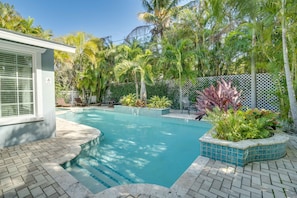 A swimming pool with a tiled edge, surrounded by a white fence, and lush tropical plants.