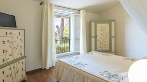 A bedroom with a bed, a dresser with floral designs, a window with curtains, and a door with floral paneling. - Casa Ciculino 8, Emma Villas (Monteleone D'orvieto)