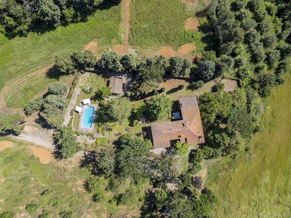 Vista aérea de una propiedad con piscina, una casa grande de techo inclinado y vegetación circundante.