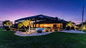 Una casa moderna con un porche cubierto, piscina y jardines bien cuidados.