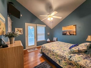 Une chambre à coucher avec un lit, un ventilateur de plafond, une porte donnant sur une vue agréable, un tableau et une plante.