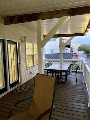 Relax on the covered porch with a table and two chairs, surrounded by the building's white exterior and dark roof.