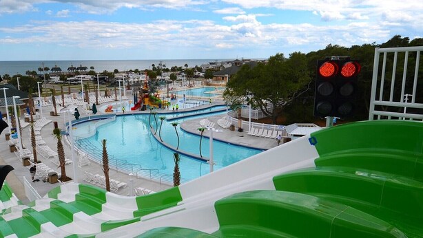 Ein Wasserpark mit mehreren Pools und Rutschen, umgeben von Palmen und Blick auf den Ozean.