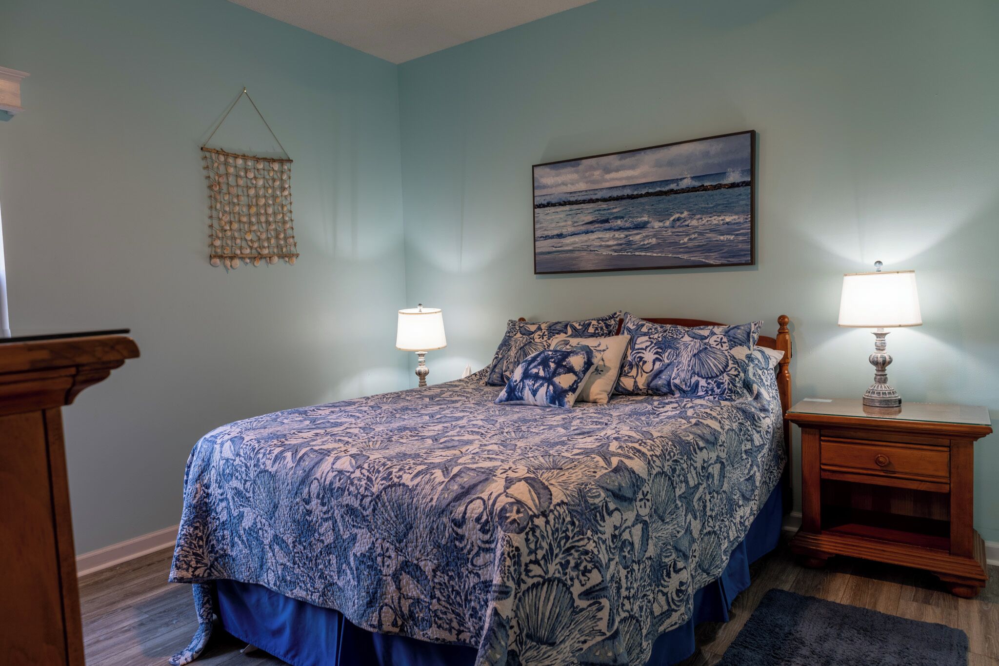 A bedroom with a large bed, two bedside tables, a hanging wall decoration, and a painting.