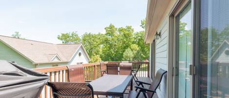 A covered outdoor patio with a table and chairs, a grill, and a view of neighboring houses and trees.