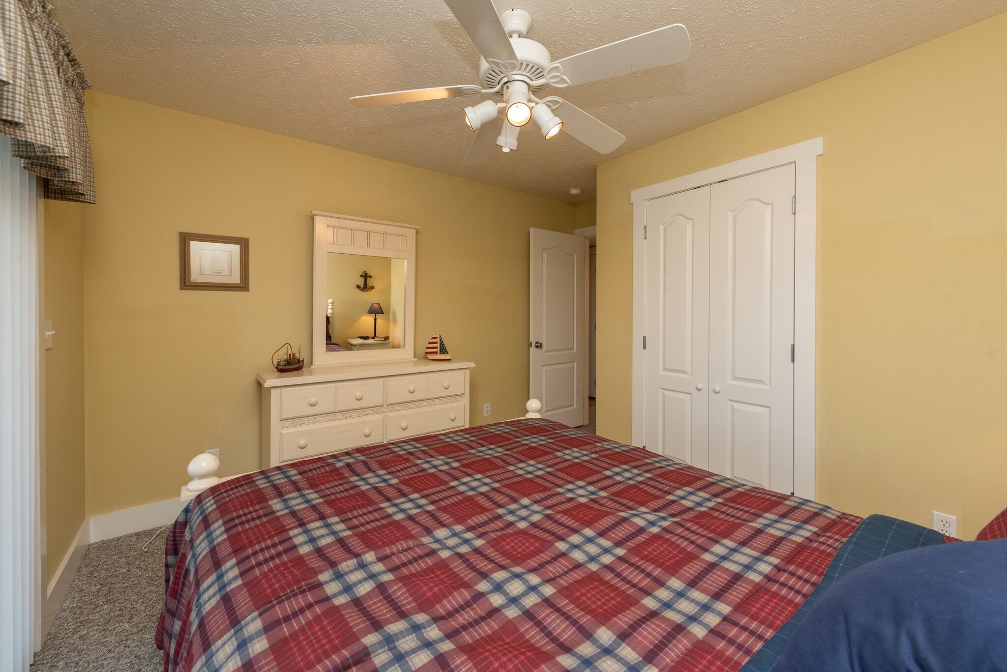 A bedroom with a bed, dresser, mirror, and a ceiling fan.