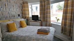 A bedroom with a bed, a bookshelf, a TV, and a window with curtains.