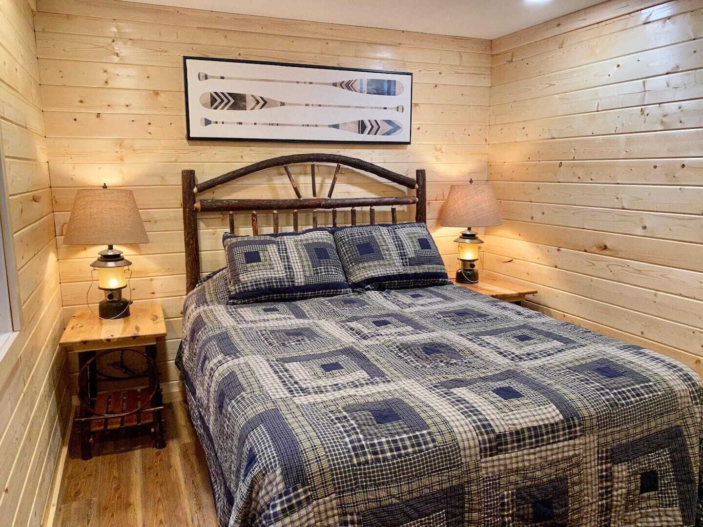 A wooden-paneled room with a bed, two bedside lamps, and a framed picture on the wall.
