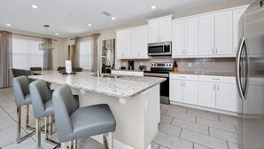 Una cocina moderna con armarios blancos, encimera de granito, electrodomésticos de acero inoxidable y una zona de bar con taburetes.