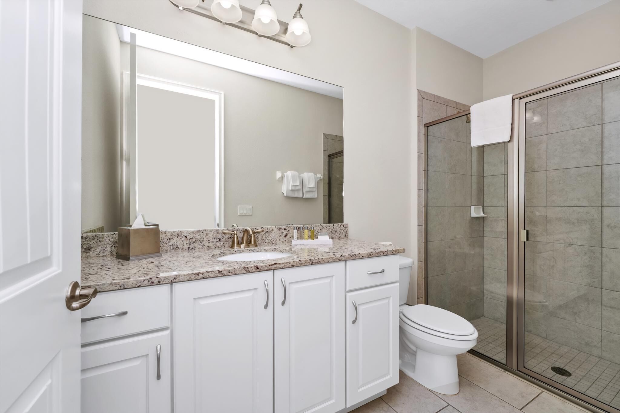 Une salle de bain moderne avec un comptoir en granit, des meubles blancs, un grand miroir, des toilettes et une douche à parois de verre.