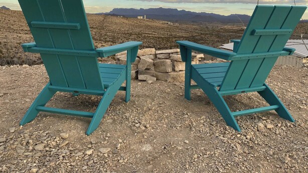 Zwei türkisblaue Adirondack-Stühle, die einem Steinkamin mit Bergblick zugewandt sind.