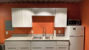 A kitchen with white cabinets, a stainless steel sink, a microwave, and a refrigerator. - Fossil Knob Ridge -Mariscal: Ultra Modern Container Home (Terlingua)