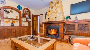 A living room with a fireplace, wooden furniture, and a TV mounted on the wall. - Cubo's Finca Las Cuatro Lunas (Alhaurin de la Torre)