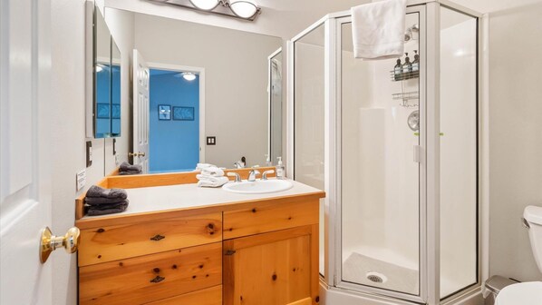 A bathroom with a wooden vanity, white sink, and a glass shower enclosure.