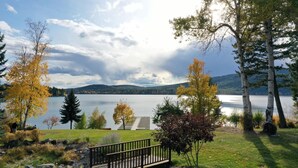 A lakeside park with a wooden deck, a small bridge, and a view of a calm lake with mountains in the background.