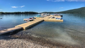 A clear lake with a dock extending into the water, surrounded by trees and hills.