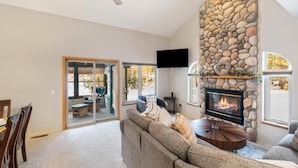 A cozy living room with a stone fireplace, a large window, and a sliding glass door leading to a balcony.