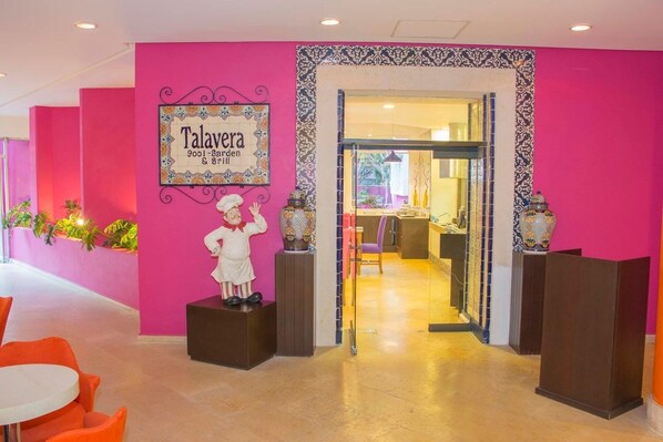 Um interior vibrante com uma estátua de chef, um letreiro para 'Talavera Pool-Sgarden & Grill' e uma porta de entrada para uma área de cozinha.