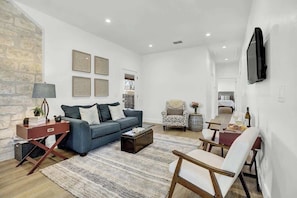 Un salon comprenant un canapé, une table basse et des fauteuils, un mur en pierre et un téléviseur fixé au mur.