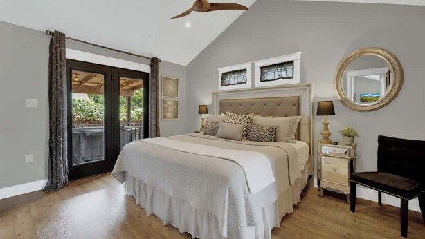 A bedroom with a large bed, a ceiling fan, a bedside table with a lamp, and a mirror on the wall.