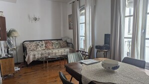 Een gezellige woonkamer met een bank, een eettafel met stoelen, een lamp en een raam met gordijnen.
