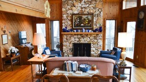 A cozy cabin interior with a stone fireplace, wooden walls, and a dining area.