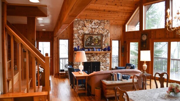 A cozy cabin interior with a stone fireplace, wooden walls, and a dining area.