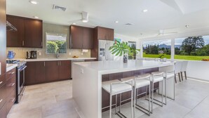 Una cucina moderna con mobili in legno scuro, una grande isola con sgabelli da bar e vista su un paesaggio verde attraverso ampie finestre.