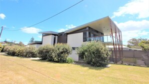 A modern two-story house with a flat roof, large windows, and a well-maintained lawn.