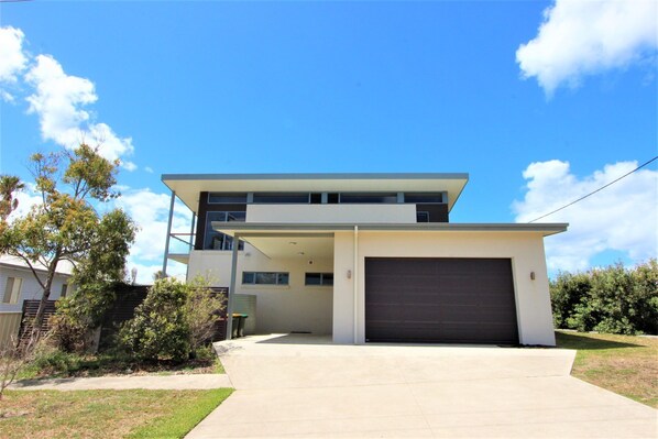 A modern two-story house with a garage, a covered driveway, and a well-maintained lawn. - The ultimate property for the family with amazing views to whale watch (Crowdy Head)