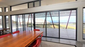 A conference room with a large wooden table and red chairs, large glass doors leading to a view of a bridge and ocean.