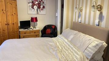A hotel room with a large bed, a wooden wardrobe, a desk with a lamp, a chair, and a wall-mounted light fixture.