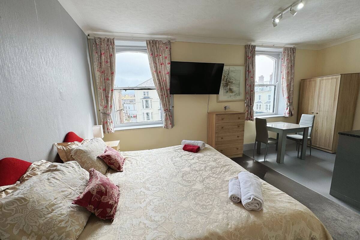 A hotel room with a bed, a desk, a chair, a wardrobe, and a TV.
