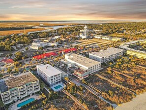 An aerial view of a resort area with multiple buildings, a swimming pool, and a bridge in the background.