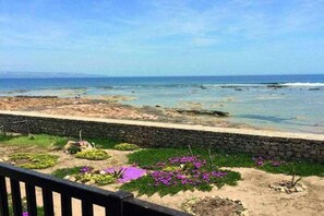 A coastal view with a stone wall and landscaped garden with purple flowers.