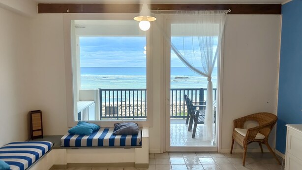 Quarto com vista para a praia, cama com roupa de cama listrada, cadeira de vime e mesa com cadeiras do lado de fora.