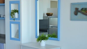 Um quarto branco com um espelho emoldurado em azul, um penteou branco com uma planta e um banco listrado.