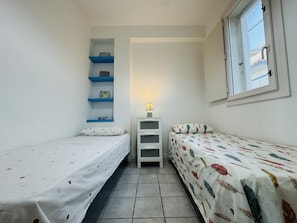 A small, clean room with two single beds, a white dresser, and a window.