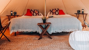 Una carpa con cama, almohadas, una mesita con lámpara y una silla.
