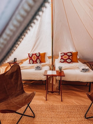 A cozy tented accommodation with two beds, each with patterned pillows, a small table, and a brown leather chair. - Wander Camp Grand Canyon (Williams)