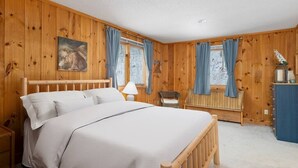 A wooden-paneled bedroom with a bed, a chair, a lamp, and a painting on the wall. - Brand New Kitchen & Bathrooms, close to Mt Snow! (Dover)