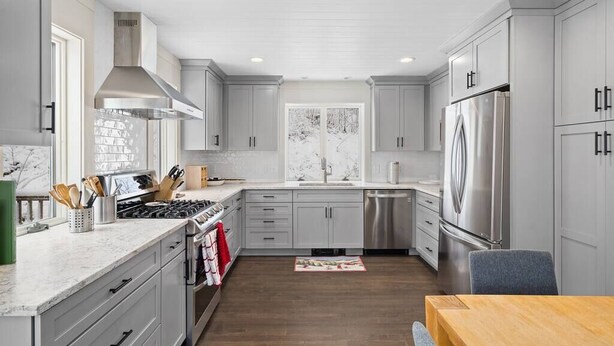 A modern kitchen with grey cabinets, stainless steel appliances, and a wooden dining table. - Brand New Kitchen & Bathrooms, close to Mt Snow! (Dover)