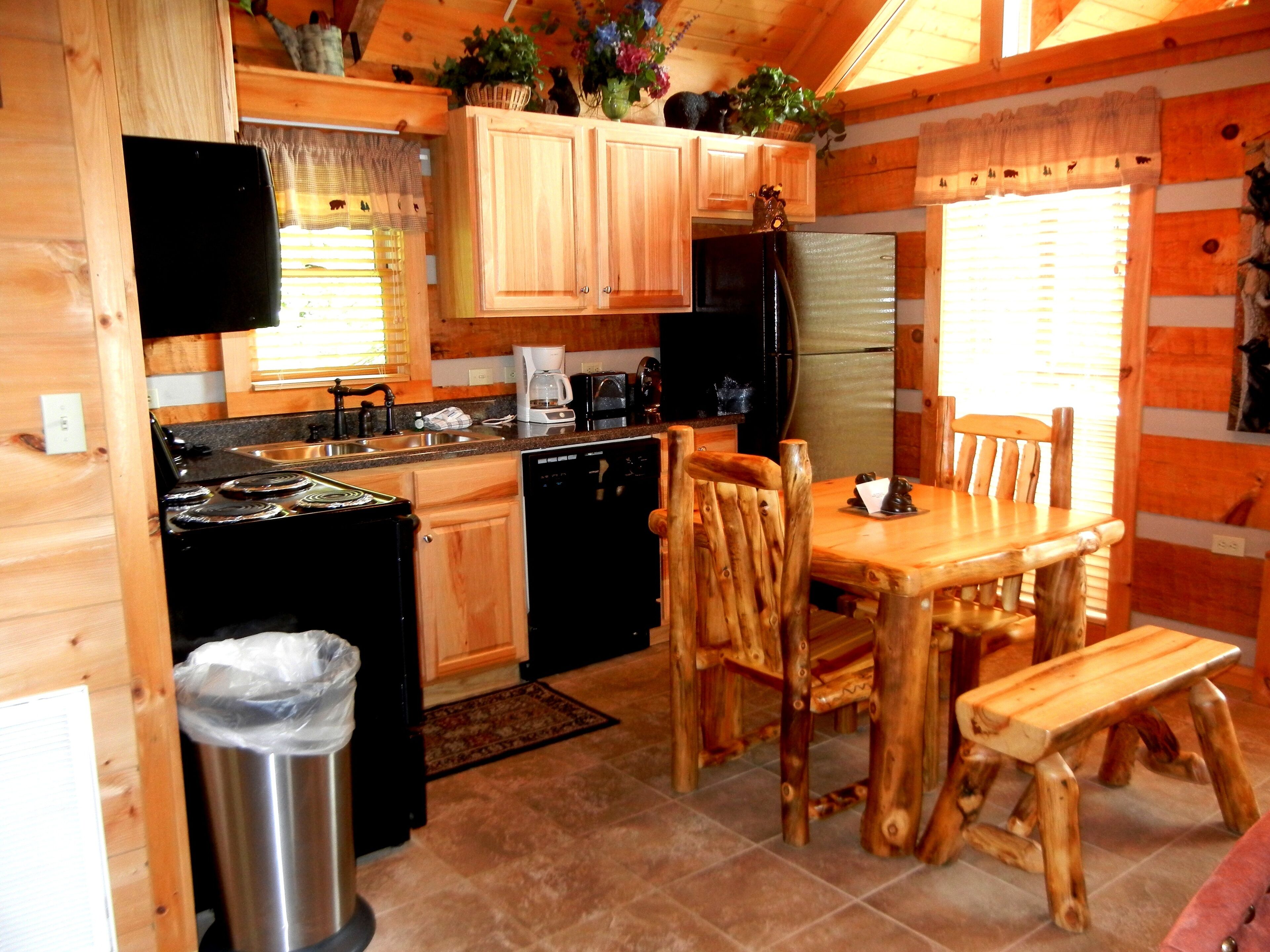 A wooden cabin-style kitchen with a dining area, including a stove, sink, refrigerator, and wooden chairs.
